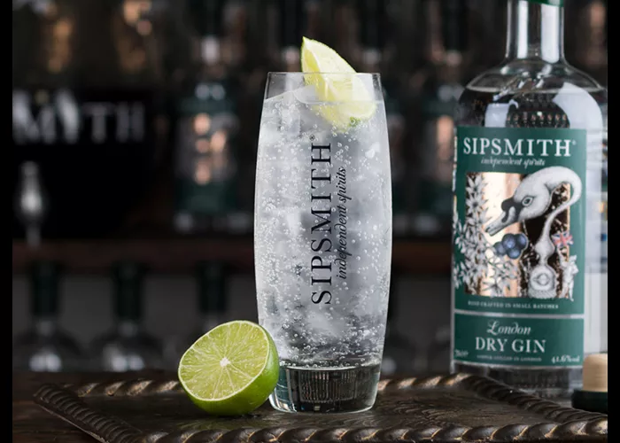 A glass if Gin & Tonic garnished with lime slice on a tray with half lime, alongside bottle of Sipsmith Dry Gin