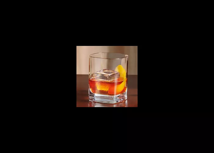 A  glass of Knob Creek® Old Fashioned on coaster alongside a peeled orange, one peeler and a bottle of knob creek whiskey