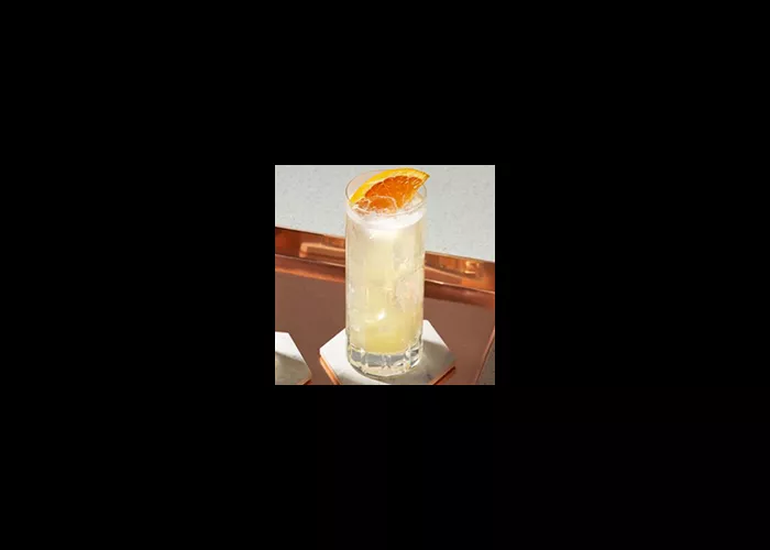 A  glass of Tom Collins garnished with chopped orange in a copper plate on a stone coaster 
