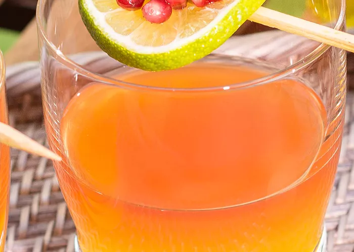 Glass of Mango Sunset garnished with a lime wheel and pomegranate seeds.