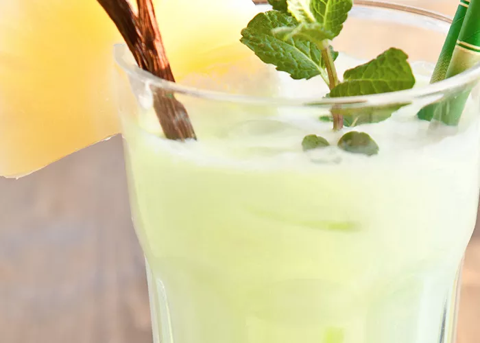 Glass of Lazy Day Colada garnished with vanilla pods, mint leaves. pineapple slice and straw