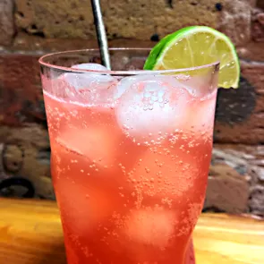 A glass of Shark's Tooth garnished with ice, lime slice and a straws