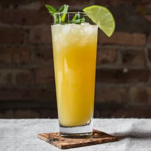 A glass of Guava Spice on a coaster, garnished with lemon slices and mint spring