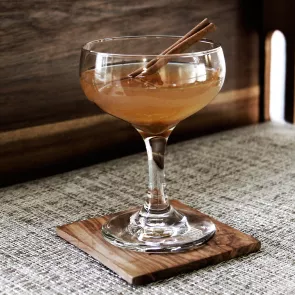 A glass of Pumpkin Bourbon Cider garnished with grated nutmeg and a cinnamon stick on a coaster.