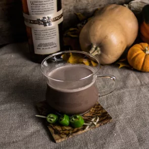 A glass of hot spiced cocoa on coaster Garnished with chilli peppers placed with some pumpkins