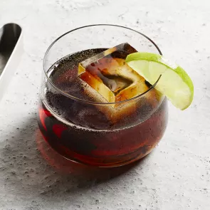 A glass of C.C.® & Cola garnished with Lime Wedge