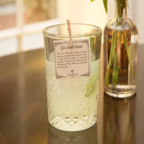 A glass of Gin Basil Smash is garnished with basil leaves and ice cubes, with a paper note attached to the rim of the glass with a clip, alongside a jar filled with water containing a basil plant.