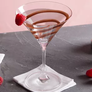 A Glass garnished with chocolate sauce and a Raspberry on rim placed on a white cloth