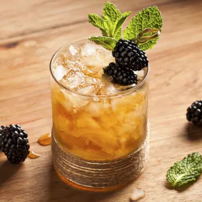 Glass of Hats Off Julep with crushed Ice, garnished with blackberries and mint leaves.