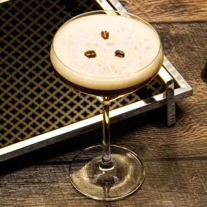 A glass of Espresso Martini garnished with coffee beans along with the tray on the table .