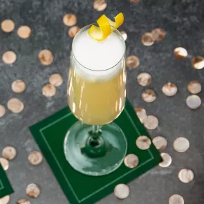  A glass of French 75 garnished with the lemon peel placed on the the green coaster