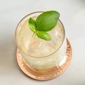 A glass of Gin Basil Smash garnished with mint leaves on a copper coaster 