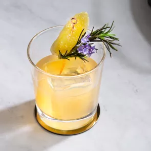 A glass of Ginger Buck  garnished with Sprig of Rosemary and Candied Ginger