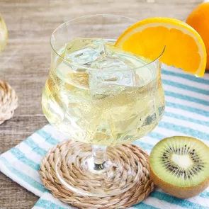 Glass of Cruzan® Daiquiri garnished with orange wedge alongside some half kiwi