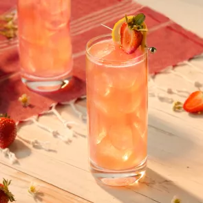 A glass of Kentucky Buck with strawsberry and lemon garnishes, placed on a wooden table next to an identical glass.