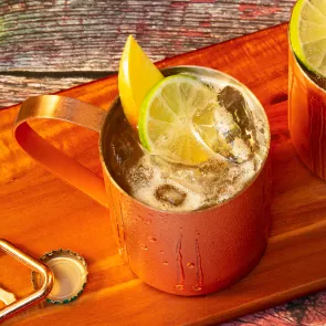 Two copper cups full of Kentucky Mule garnished with mango and sweet lemon  placed on a wooden frame