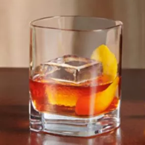 A  glass of Knob Creek® Old Fashioned on coaster alongside a peeled orange, one peeler and a bottle of knob creek whiskey