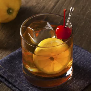 Glass of Maker's Mark® Sour garnished with ice, lemon slice and cherry placed on a blue cloth.