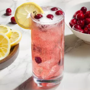 A glass of Maker's Mark® Merry Berry Buck garnished with Cranberries and lemons