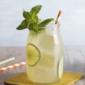 A jar of Handsome Ginger garnished with mint leaves, lime slices and straws on a yellow coaster