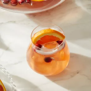 A glass of Pinnacle® Holly Jolly Punch garnished with Orange slice and Cranberries 