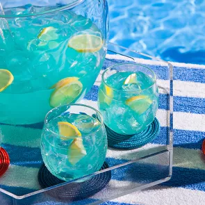 A tray with two glasses and a summer fish bowl containing a Ice-cold drink garnished with lemon.