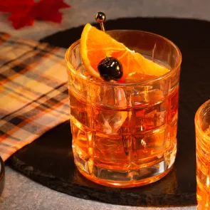 A  glass of Smoked Maple Old Fashioned garnished with Orange Slice and Cherries 