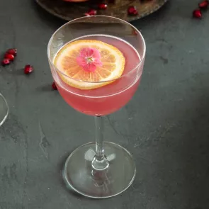 A glass of Tickled Pink garnished with Lemon, Orange and Edible Flowers 