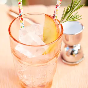 Glass of Peachy Keen garnished with peach slice and rosemerry with a straw