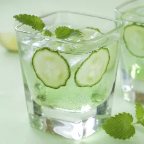 A glass of Cucumber Martini garnished with mint leaves, cucumber wheel and ice cubes