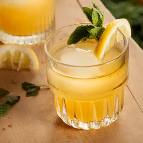 A glass of Cruzan® 9 Tea garnished with lemon wedge and mint leaves with some of them fallen alongside.