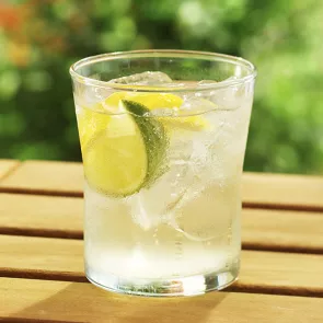 A glass of Light and Tonic placed on wooden table, garnished with a lime wedge.