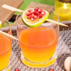 Glass of Mango Sunset garnished with a lime wheel and pomegranate seeds.