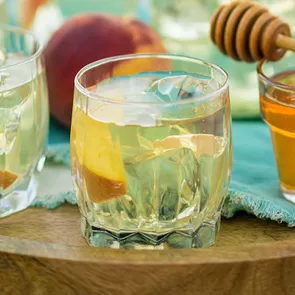 A pitcher of Paradise Punch placed with two glasses containing lemon juice and honey syrup  with wood honey dipper stick placed on top of glass.  