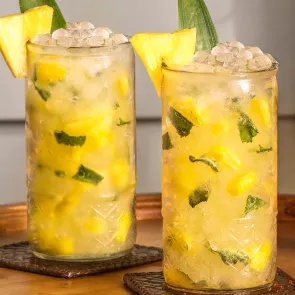 Two glasses of Pineapple Crush garnished with crushed ice and pineapple slice and a leaf