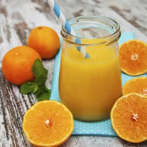 A mug glass of Smashin' Passion along with couple of oranges, some halved oranges, few mint leaves. And a straw in the mug .