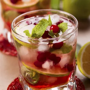 Glass of Spiced Holly Highball garnished with mint leaves and cranberries