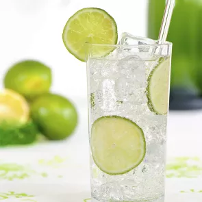 A glass of Cruzan® Summer Breeze with ice cube, topped with sparkling soda water, garnished with a lime wedge on the rim, and a straws.