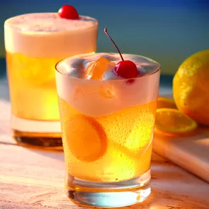 Two glasses of Amaretto Stone Sour, each garnished  with a cherry, ice cubes, and an orange slice.