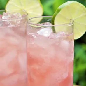 Two glass of Blushing Margarita garnished with  ice cubes and the wheel of lemon on rim