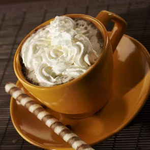 A mug of Buttershots™ Slide hot coffee, garnished with whipped cream, is placed on a coaster