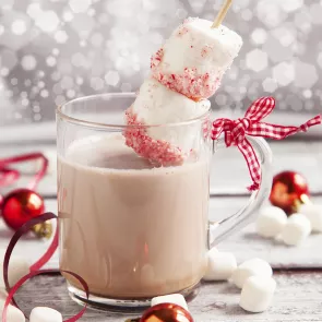 A mug of Christmas Mint Kiss, garnished with two marshmallows pierced on a toothpick and a bow tied to the handle of the cup.