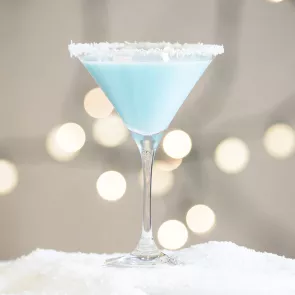 A glass of Coconut Snowball Martini garnished with honey and shredded coconut around the rim.