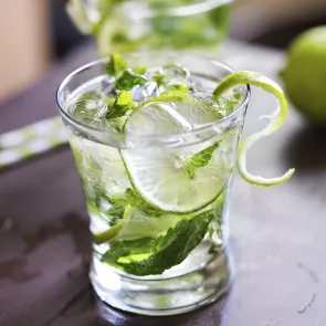 Glass of Home Team Mojito with ice, mint leaves, lime wheel, and garnished with lime peel.