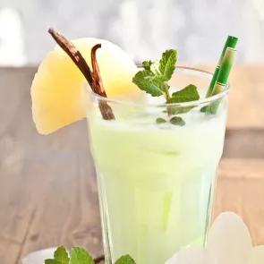 Glass of Lazy Day Colada garnished with vanilla pods, mint leaves. pineapple slice and straw