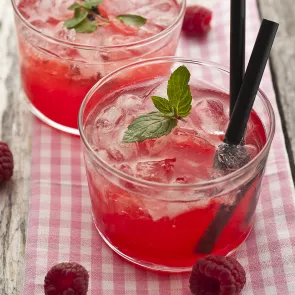 Two glasses of Sauza® Razzmatazz Margarita with two black straws in it garnished with mint leaves alongside few raspberries.