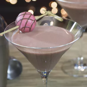 A glass of Razzmatazz® Truffle Martini garnished with a chocolate ball pierced on a cocktail pick on the rim.