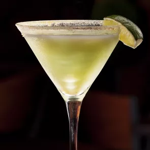 A glass of Sour Apple Popsicle Martini garnished with a slice of lime and crushed sugar on the rim