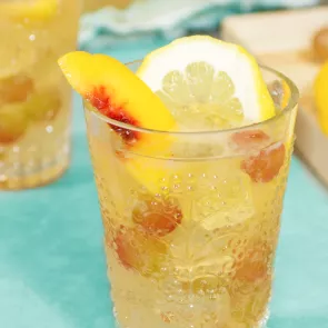 A glass of Spring Sangria garnished with lemon wheel, peaches and grapes