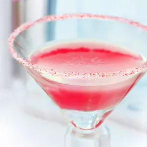 Glass of Sugar Pop Martini garnished with a rim rimmed with lemon juice and dipped in carbonated candy.